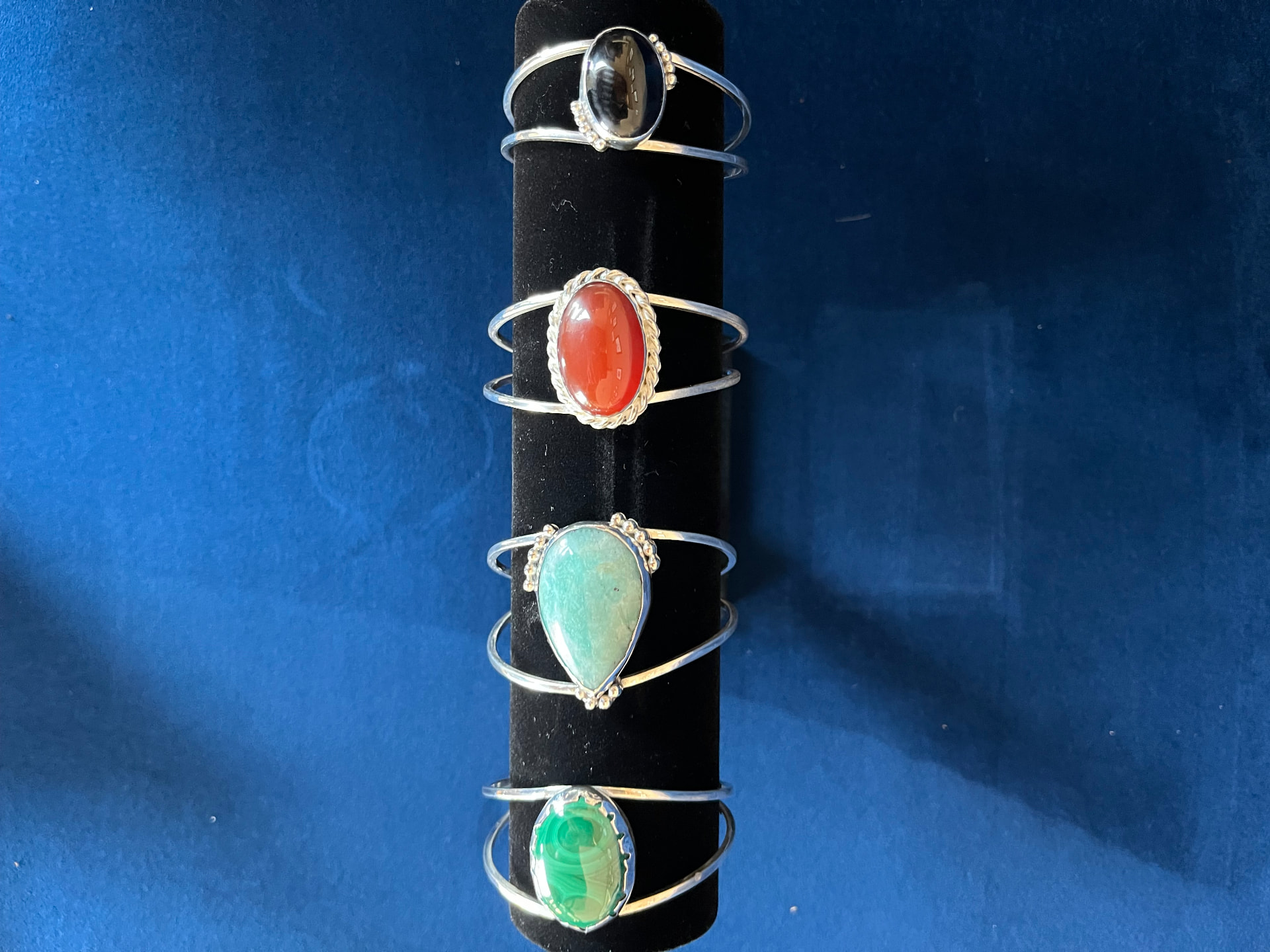 Four handmade sterling silver cuff bracelets on a black display stand, set with black onyx, carnelian, amazonite and malachite cabochons in hand-raised bezels — Giovanni Jewelers, Portland, Oregon